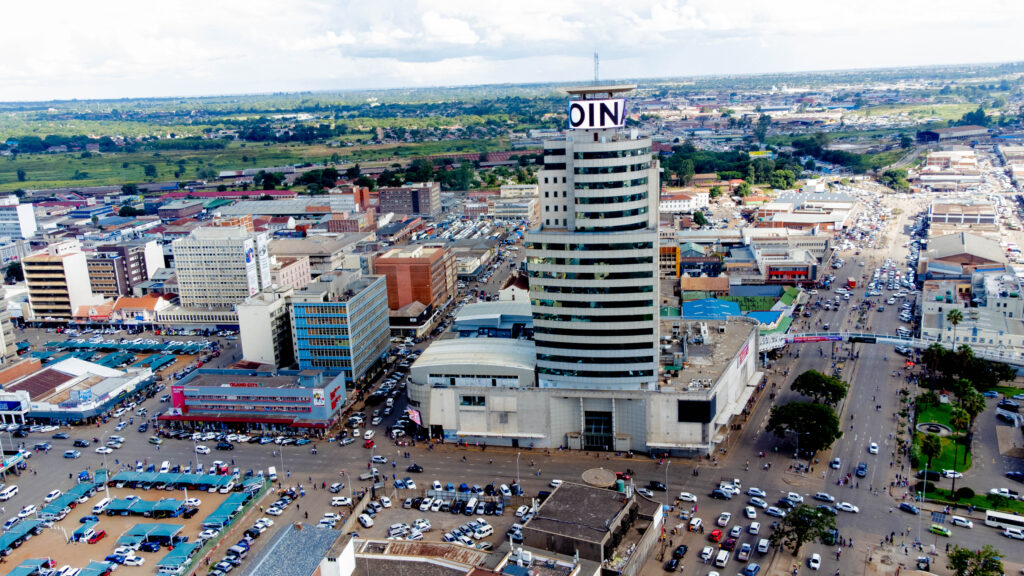 Comprehensive city-scale media project for Joina City, Harare. Wide-angle aerial drone shot capturing the iconic skyscraper and retail complex integrated into the city's central business district at sunset