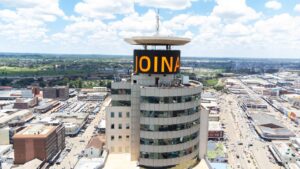 Aerial drone photography of Joina City in Harare, featuring the large curved LED digital billboard at the top displaying the "JOINA" logo. Announcement video thumbnail for Kakic Business digital screen projects